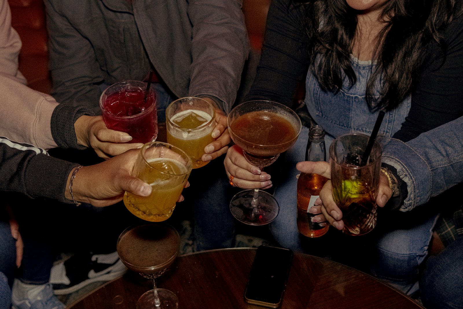 Guests raising glasses together across a table in a low-lit bar.