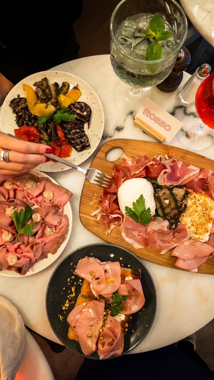 A board of cured meats and cheese with a hand reaching in.