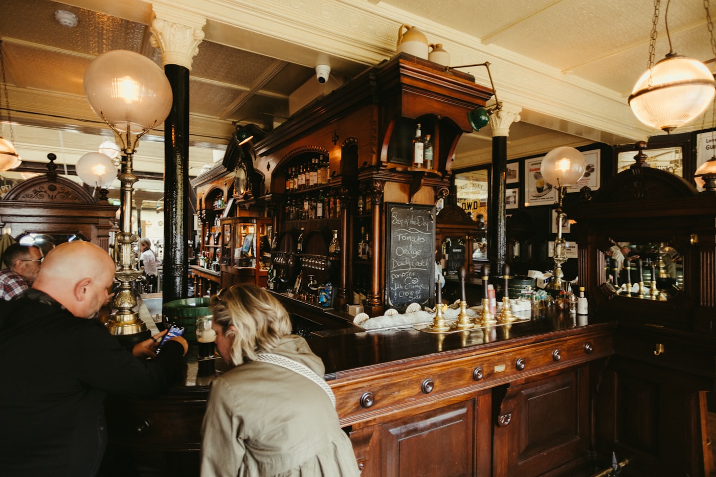 Guests standing at the ornate wooden bar of a traditional pub.